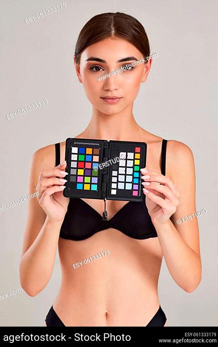 female model holds colorchecker passport in her hands for correct color transfer during further color correction on studio background