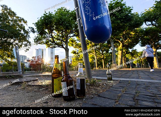 09 June 2022, Hessen, Frankfurt/Main: Empty and drunk glass bottles stand under a trash can on Schaumankai. Pizza boxes, coffee cups
