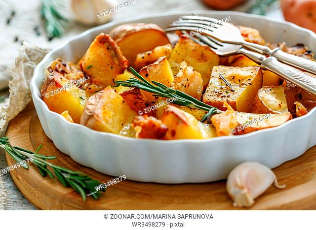 Sliced potatoes baked with bacon, rosemary and garlic in a white ceramic form, selective focus