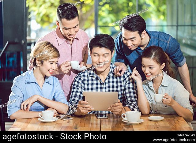 Group of smiling friends looking at digital tablet sitting in the coffee shop