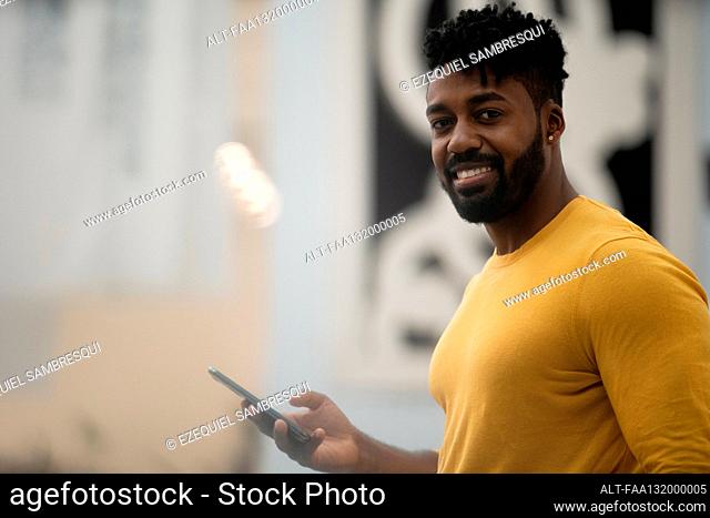 African American man looking at the camera while holding smart phone