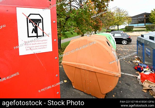 07 November 2022, Baden-Wuerttemberg, Weinstadt: A used clothing container (l) with a sign reading ""Danger to life when entering"" is located in a parking lot