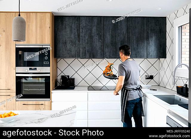 Man tossing vegetables in cooking pan preparing food at home