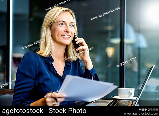 Smiling businesswoman talking on smart phone at table in cafe