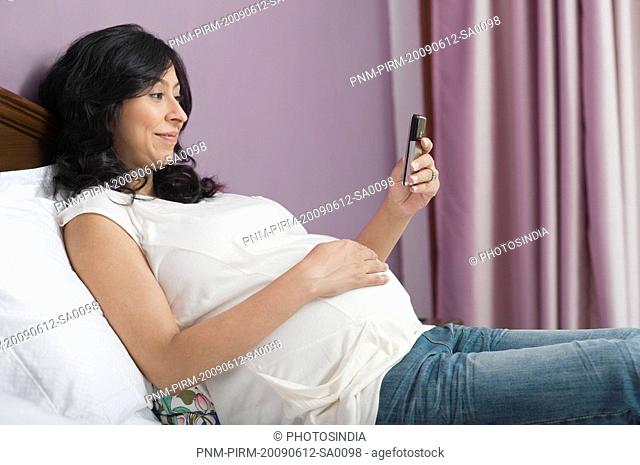 Pregnant woman touching her abdomen and text messaging on a mobile phone
