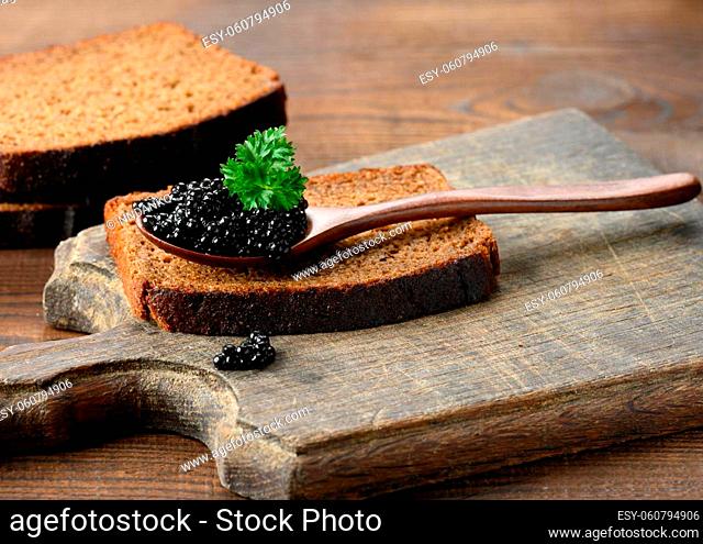 fresh grainy black paddlefish caviar in brown wooden spoon on a brown table, close up