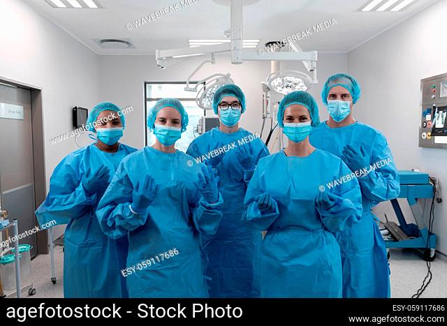 Diverse group of male and female surgeons standing in operating theatre wearing protective overalls