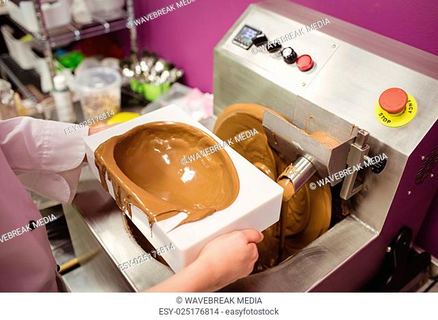 Mid section of worker filling mould with melted chocolate