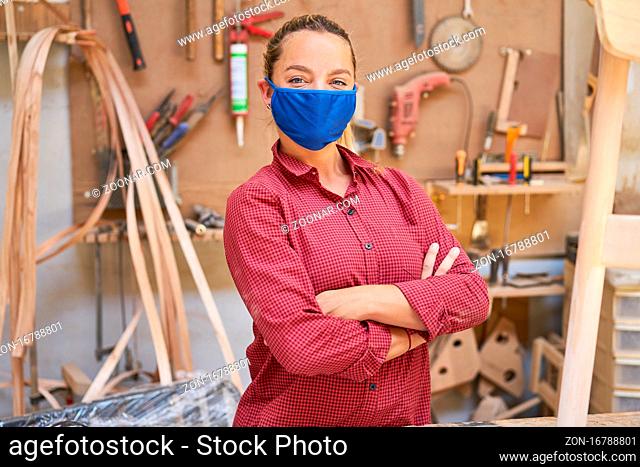 Junge Frau als Handwerker Azubi mit Mundschutz wegen Covid-19 in der Werkstatt