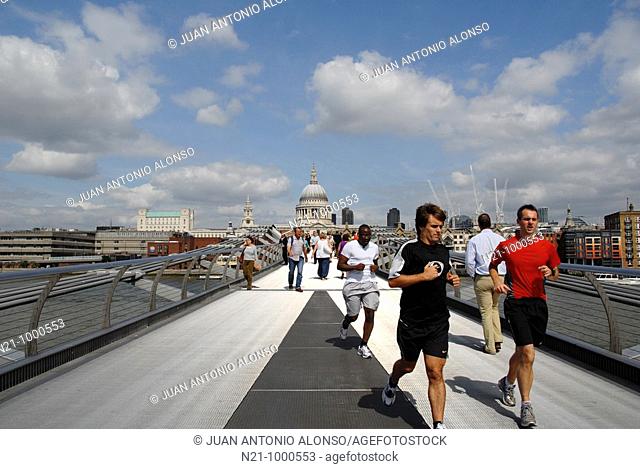 Pedestrians and joggers on Norman Foster’s Millenium Bridge over the river Thames. Saint Paul’s Cathedral is in the backlground