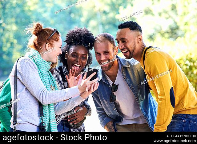 Happy young friends using smartphone in public park