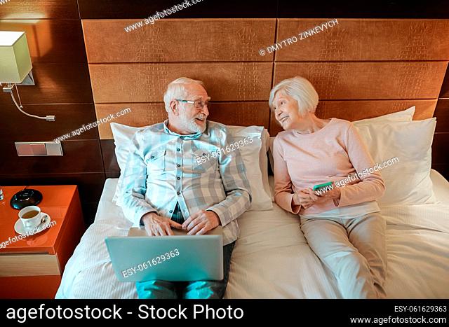 Resting in a hotel. Senior couple lying on bed in a hotel room and watching something online