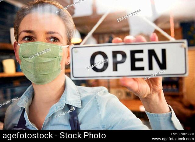 Female Owner Of Small Business Wearing Face Mask Turning Round Open Sign During Health Pandemic