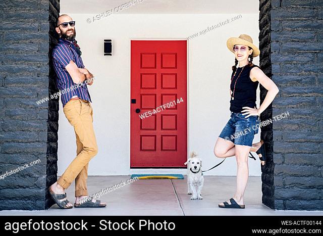Mid adult couple and Maltipoo dog standing in front of house
