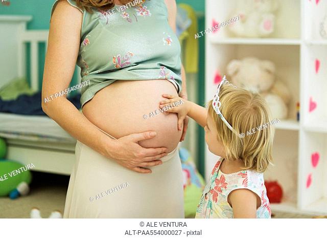 Little girl touching mother's pregnant belly