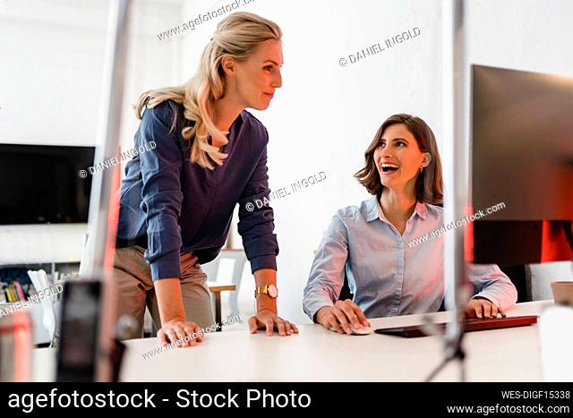 Cheerful female professional looking at businesswoman while discussing at office