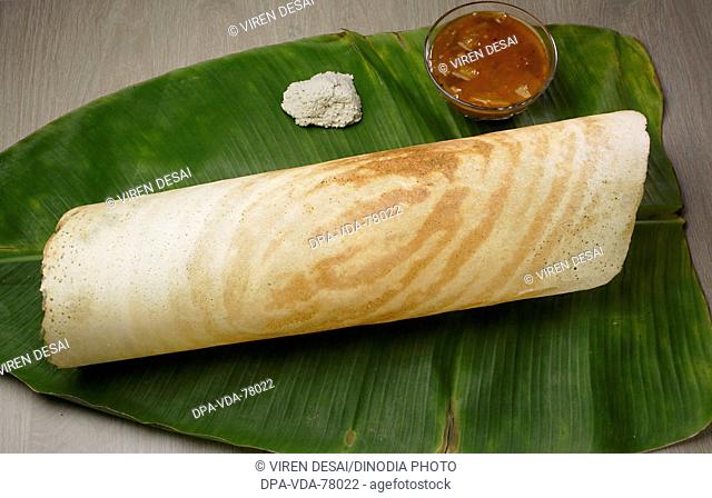 Indian snack food dosa with chutney and sambhar on a coconut leaf