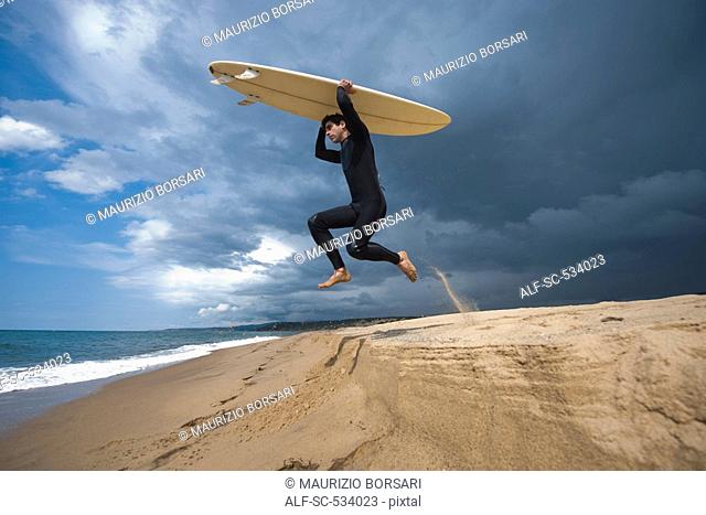 Surfer carrying surfboard on head and jumping up in air