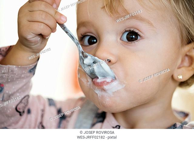 Portrait of baby girl eating yogurt, close-up