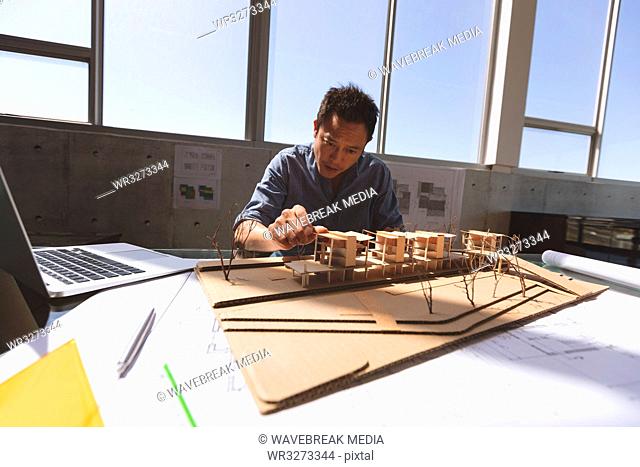 Male architect working on architectural model at desk in a modern office