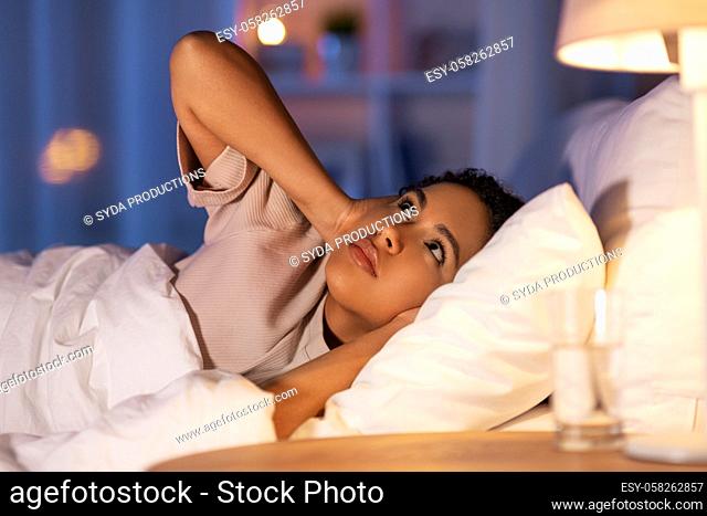 angry african woman lying in bed and closing ears