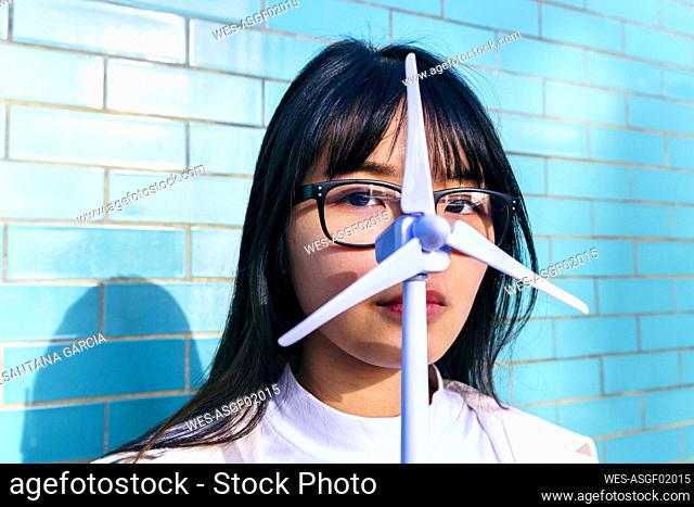 Young woman with eyeglasses holding wind turbine toy in front of face