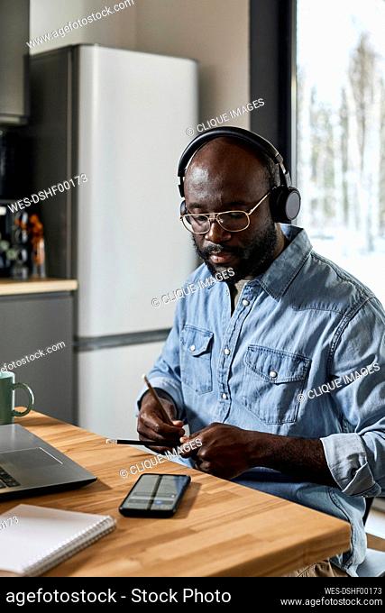 Man with headphones playing rhythm using pencils on dining table at home