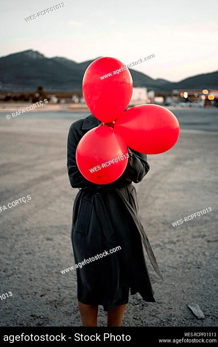 Mid adult woman covering face with red balloon while standing at road