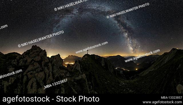 Panorama of the Milky Way with the summit cross of the Grubigstein near Lermoos. In the background you can see the Zugspitze glowing between the mountains
