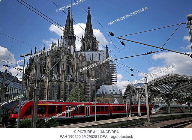 14 May 2019, North Rhine-Westphalia, Cologne: A train from the direction of the main station passes the cathedral. The cathedral and the main station are close...