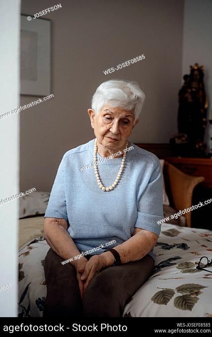 Worried senior woman sitting on bed at home
