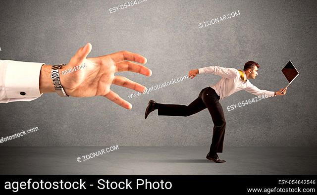 Young miniature businessman running from a big hand with light grey background
