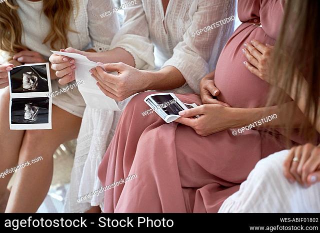 Hands of pregnant woman with friends holding ultrasound scan result at baby shower