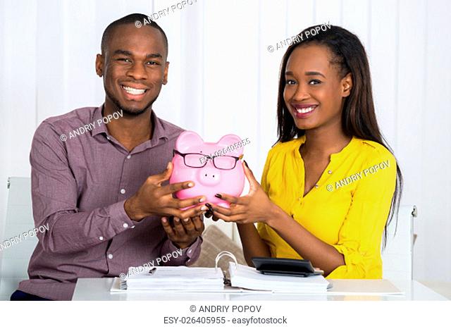 Happy Couple Holding Piggybank With Invoice And Calculator On Desk