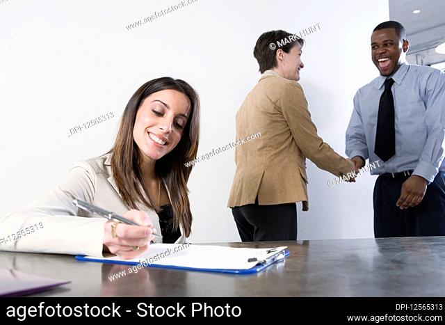 Business woman writing with business colleagues shaking hands in background