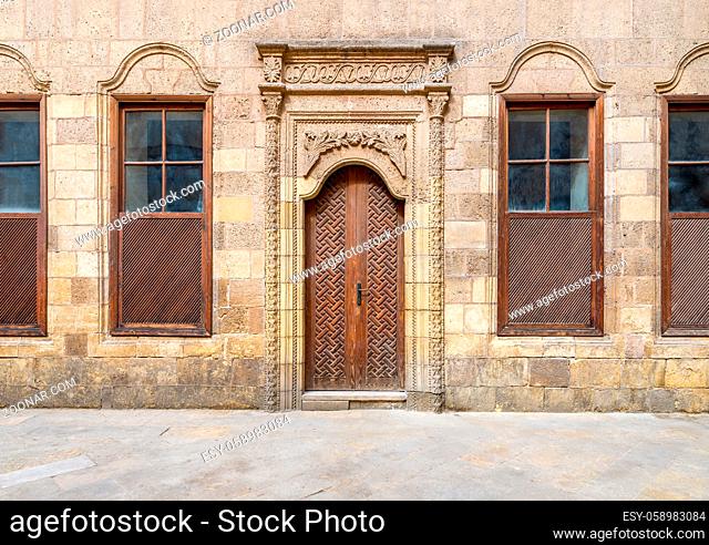 Facade of old abandoned stone decorated bricks wall with arched wooden door and four wooden shutter windows