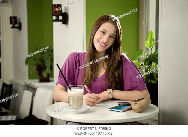 Germany, Bavaria, Munich, Portrait of young woman writing postcard in cafe, smiling