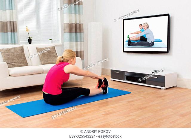 Young Woman Exercising While Watching Program On Television At Home