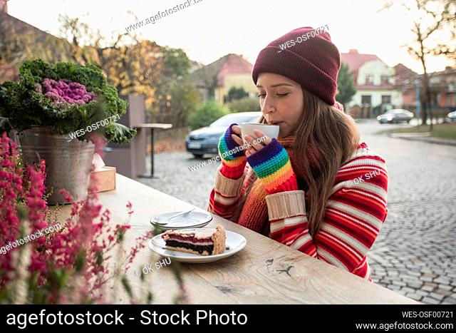 Woman wearing knit hat drinking coffee at sidewalk cafe