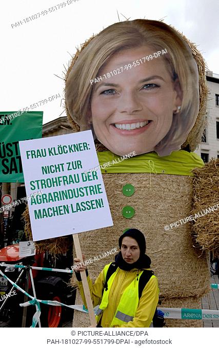 27 October 2018, Berlin: A demonstrator standing with a poster with the inscription ""Frau Kloeckner: Nicht zum Strohfrau der Agrarindustrie machen lassen""...