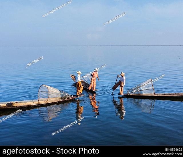 Myanmar travel attraction landmark, three traditional Burmese fishermen with fishing nets on boats at Inle lake in Myanmar famous for their distinctive one...