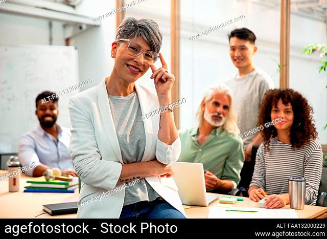 Agency manager sitting on table while looking at the camera