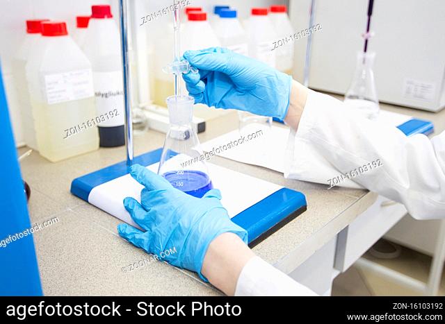 The hands of a technician in blue rubber gloves are holding a flask. Pharmaceutical industry. Chemical laboratory