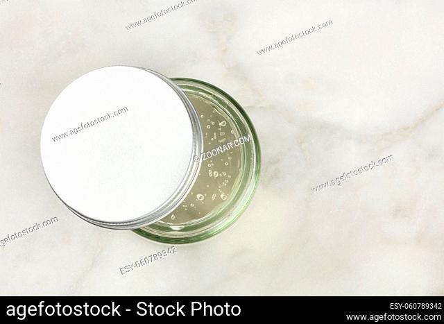 An overhead photo of a glass jar with aloe vera gel, shot from the top on a white marble background with a place for text