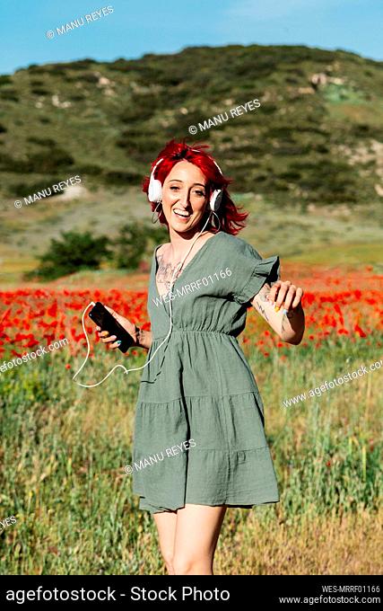 Happy woman enjoying music on poppy field during sunny day