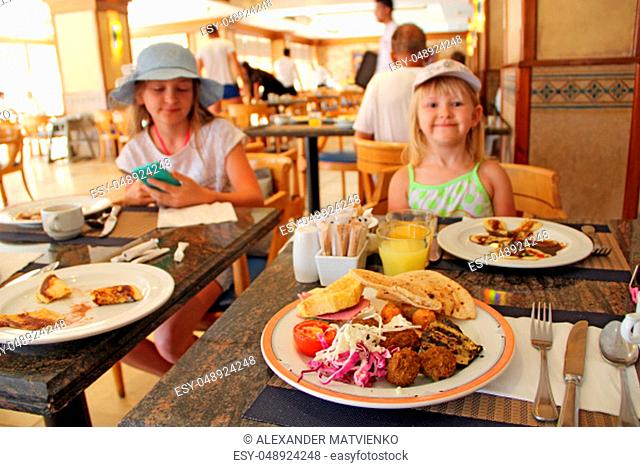 Children eating lunch with fresh vegetables, meaty dishes at restaurant. Modern children tourists eat dishes in restaurant