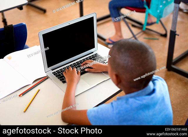 African american boy using laptop while sitting on his desk in the class at elementary school