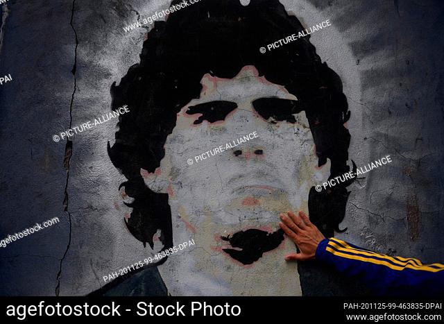 25 November 2020, Argentina, Buenos Aires: A fan of the football club Boca Juniors puts his hand on a mural with the picture of the football star Diego Maradona...