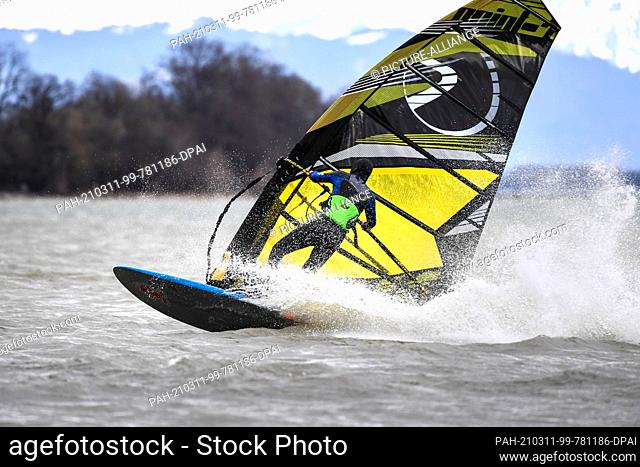 11 March 2021, Baden-Wuerttemberg, Friedrichshafen: A surfer jumps with his surfboard over Lake Constance in front of Fischbach