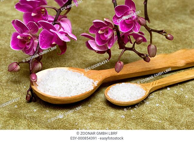 Spa essentials bath salt in a spoon and flowers of orchids